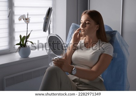 Young beautiful female customer with mirror getting ready for beauty procedures in a medical salon Royalty-Free Stock Photo #2282971349