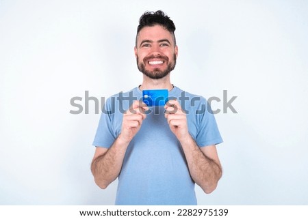 Photo of Young caucasian man wearing blue t-shirt over white background positive smile hold credit card income salary