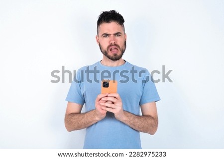 Photo of interested Young caucasian man wearing blue t-shirt over white background hold telephone look side empty space screen