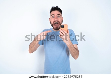 Portrait cute astonished Young caucasian man wearing blue t-shirt over white background impressed unbelievable unexpected incredible notification advice