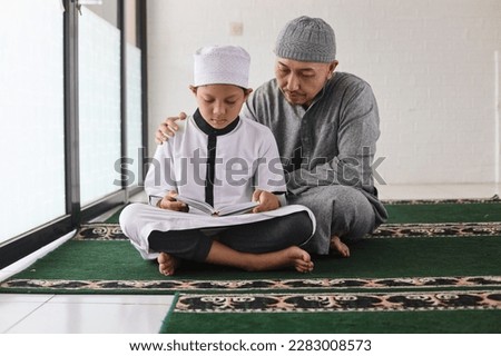 Portrait of happy Muslim father teaching son reading the Quran and praying together at mosque.  Royalty-Free Stock Photo #2283008573