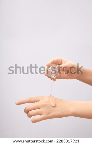 Front view of female hand pouring transparent essence on back of other hand on light background. Mockup scene for cosmetic product, daily skin care routine. Royalty-Free Stock Photo #2283017921