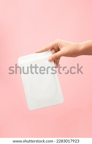 Front view of female hand holding a facial sheet mask packaging mockup on pink background. Scenes advertising beauty products, moisturizing masks, whitening for skin care. Royalty-Free Stock Photo #2283017923