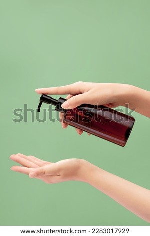 Cosmetic transparent plastic bottle with dispenser pump is carried by woman hand model. Cosmetic product branding mockup