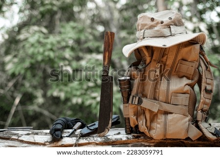 Equipment for survival bucket hat backpack hiking knife camping flashlight resting on wooden timber in the background is a jungle Royalty-Free Stock Photo #2283059791