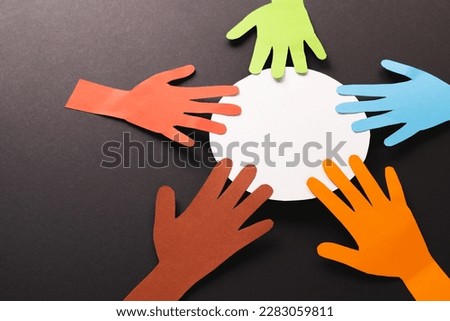 Paper cut out of multi coloured hands and white circle with copy space on black background. Humanitarian, people, help and human concept.