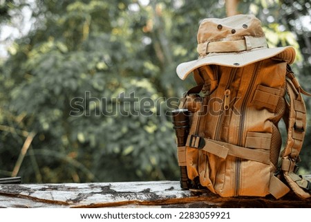 Bucket Hat and backpack hiking with a flashlight resting on wooden timber in the background is a forest