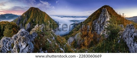 Mountains in low clouds at sunrise in autumn. View of mountain peak in fog in fall. Beautiful landscape with rocks, forest, sun, purple sky. Top view of mountain valley in clouds. Foggy hills Royalty-Free Stock Photo #2283060669