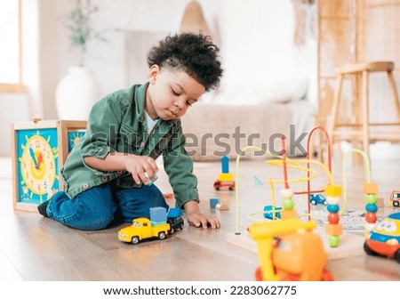 Concentrated little african american boy playing toys sitting on warm floor in modern living room. Baby development. Small tower. Learning creative concept Royalty-Free Stock Photo #2283062775