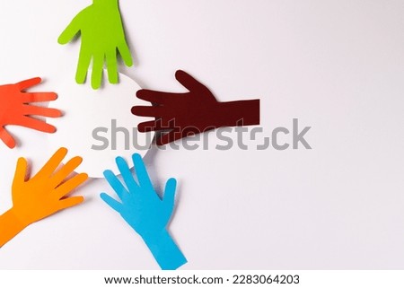 Paper cut out of multi coloured hands and white circle with copy space on white background. Humanitarian aid, people, help and human concept.