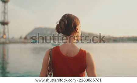 Girl stands on the embankment and looks at the bay. Young woman looks at the sea in the morning time. Back view Royalty-Free Stock Photo #2283065761