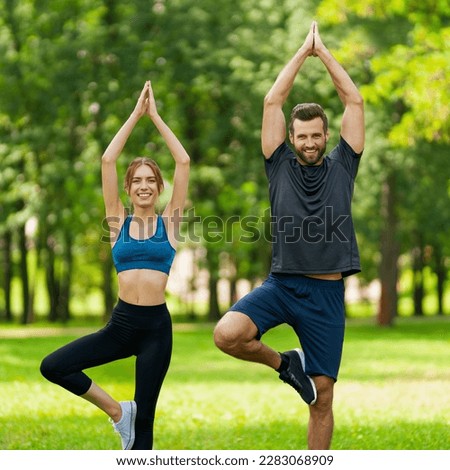 Full body image - smiling couple  stand in asanas position or woman practicing with man, male bearded coach trainer, do yoga exercises, meditating together, after outside training. Square composition.