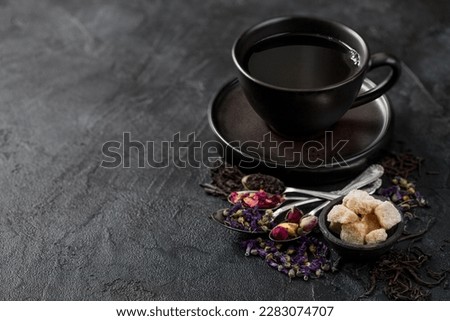 Tea cup with spoons and various tea on black. Black and green loose tea,rose buds,blue mallow flowers