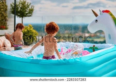 excited kids having fun in inflatable pool on summer patio. jumping and splashing around Royalty-Free Stock Photo #2283107283