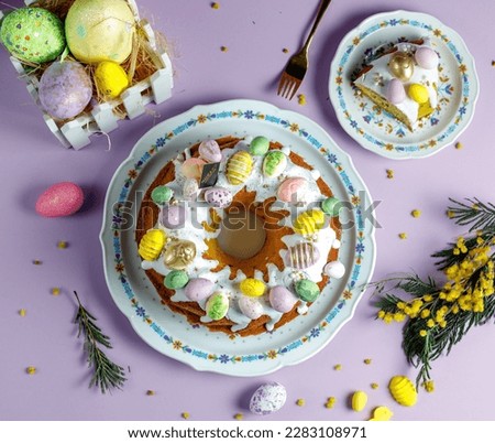 Ester cake with glaze and colored little eggs, slice of cake in plate with flowers.
