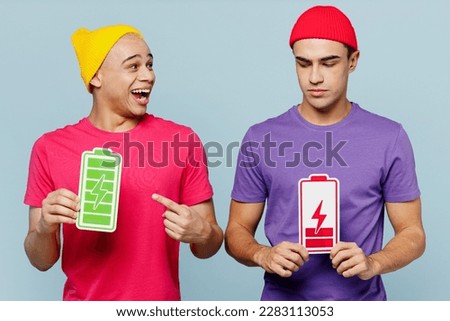Young smiling happy couple two friends men wear casual clothes together hold in hands point on green red charge battery card sign isolated on pastel plain light blue cyan background studio portrait Royalty-Free Stock Photo #2283113053
