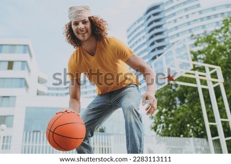 Bottom view young happy fun cool man 20s wearing yellow t-shirt bandana playing basketball on playground in free time walking rest relax in city outdoors on open air. Urban lifestyle leisure concept