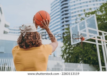 Back rear view young caucasian man in yellow t-shirt bandana hold ball shooting playing basketball on playground in free time rest relax in city outdoors on open air. Urban lifestyle leisure concept