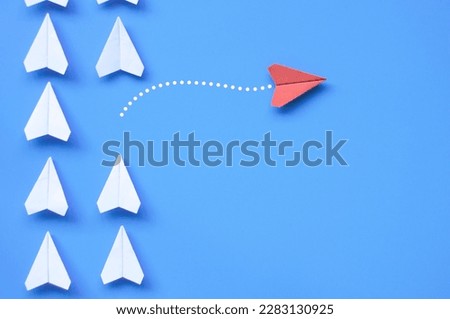 Top view of red paper airplane origami leaving other white airplanes on blue background with customizable space for text or ideas. Leadership skills concept. Royalty-Free Stock Photo #2283130925