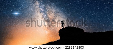 Lone person standing on top of rock, pointing with hand towards the Milky Way and the vast expanse of universe. Stunning silhouette of man gazing out into the cosmos. Power of dreams and aspirations. Royalty-Free Stock Photo #2283142803