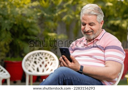 Happy senior man sitting at garden and using smartphone. Royalty-Free Stock Photo #2283156293