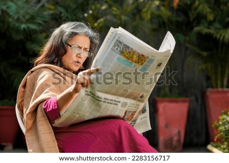 Relaxed senior woman sitting on chair at out of home reading newspaper.