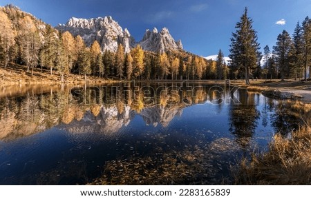 Incredible autumn scenery with reflections. Amazing autumn landscape in the mountains with yellow larches and lake glowing by sun and high mountain peaks behind. Picture of Wild area. Wallpaper
