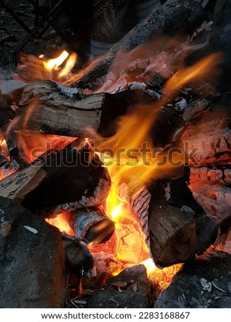 Campfire, coals, embers, big stones, and people around the fire, relaxing in the evening