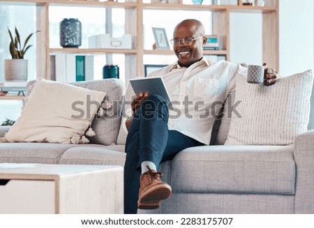 Tablet, coffee break and relax with a black man on the sofa, sitting in the living room of his home or office. Business, tech or research with a male employee reading an online article while chilling Royalty-Free Stock Photo #2283175707