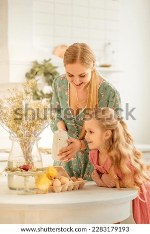 Happy little girl with mom and little ducklings. Family portrait of an adorable little girl of preschool or school age with her mother. Mom holds a fluffy duckling with both hands, kisses her daughter