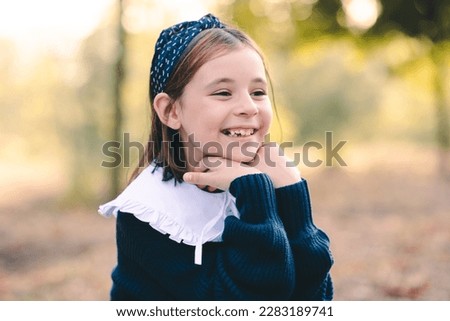 Smiling funny kid girl 6-7 year old wear school uniform dress with white collar outdoor over nature background closeup. Childhood. Back to school.  Royalty-Free Stock Photo #2283189741