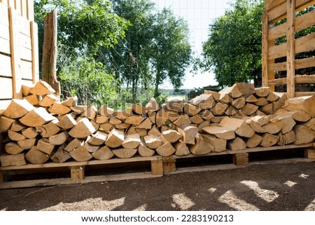 Pile of firewood in the summer stocked outdoors in a shed, being prepared for winter