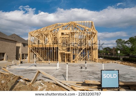 Unfinished new development wooden two-story houses with sold sign near completed homes, beam truss frame, slab foundation, utilities plumbing pipeline installation. Suburban housing Irving, Texas, US