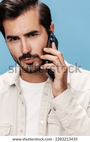 Portrait of male brunette anger talking on the phone in close-up, disgruntled, on a blue background in a white T-shirt and jeans, copy space