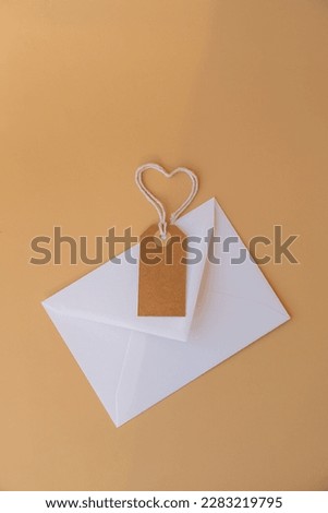 White envelope with beige paper note and rope in heart shape on neutral beige background. Greeting card holiday idea. Mock up copy space for text