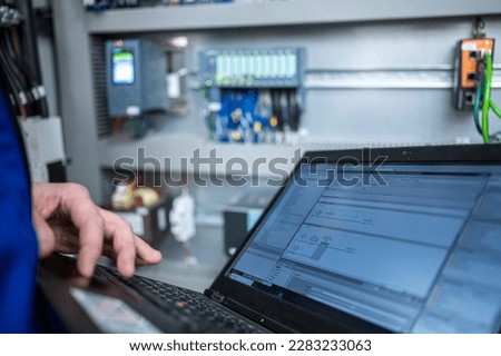 Programmer of PLC checks correct function of program in PLC with electrical cabinet in background Royalty-Free Stock Photo #2283233063