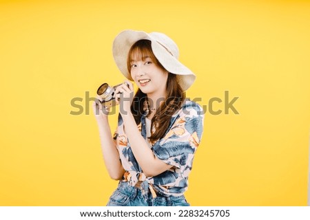 A woman in a hat holds a film camera in front of a yellow background