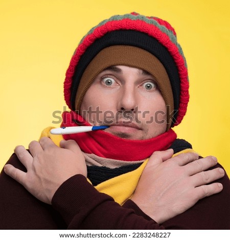 A young man in warm clothes on a yellow background holds an electronic thermometer in his mouth and is shocked by the high temperature Royalty-Free Stock Photo #2283248227