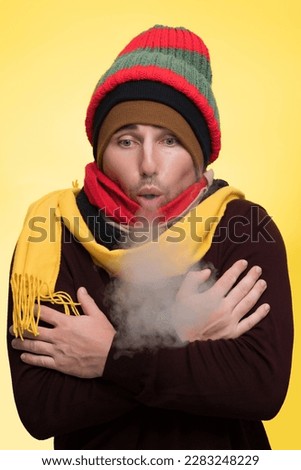 A man in warm clothes and several hats warms himself during the cold and steam comes from his mouth Royalty-Free Stock Photo #2283248229