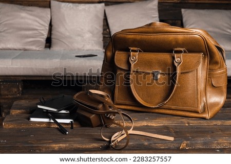 Brown leather bags with men's accessories on wooden table over home background