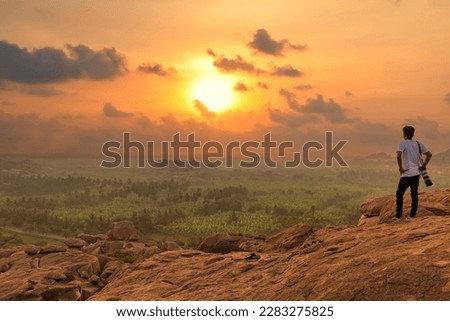 Male tourist photographer enjoys a scenic sunset view from a hill top at Hampi, Karnataka, India