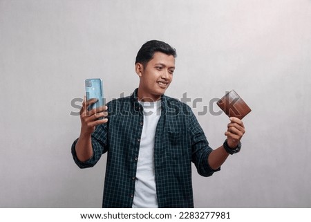 Mature man in green shirt smiling happily holding mobile phone and showing brown wallet, isolated on white