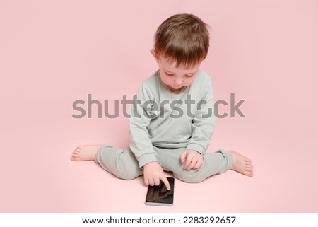 Happy toddler baby with mobile phone on studio pink background. Child boy holding a smartphone in his hands. Kid age one year eight months, full height