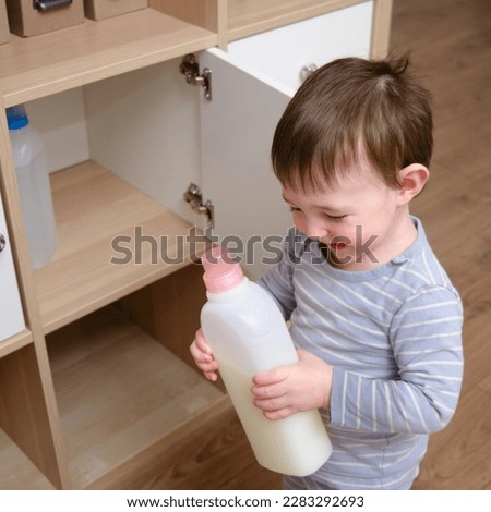 Toddler baby plays with household chemicals and detergent from the closet. Child boy with detergent bottle in home living room. Kid age one year nine months