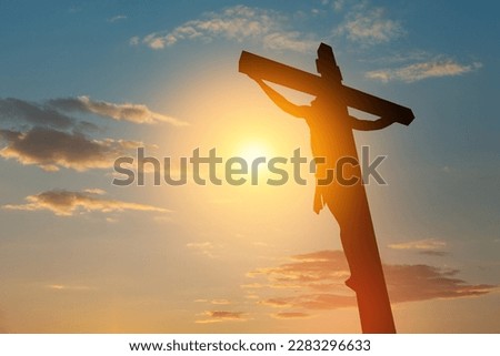 Silhouette of the crucified Jesus Christ on the cross on background of sunset sky.