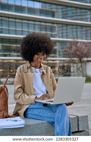 Vertical photo of happy female student using of pc laptop outdoors. An African American female business freelancer entrepreneur using app project for online work sitting in front of business buildings