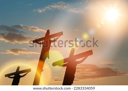 Silhouette of the crucified Jesus Christ on the cross along with other people on background of sunset sky.