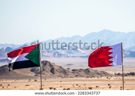Sudanese and Bahrain flags waving togetner on the wind in Saudi Arabian desertwith mountains in background, Al Ula, Saudi Arabia