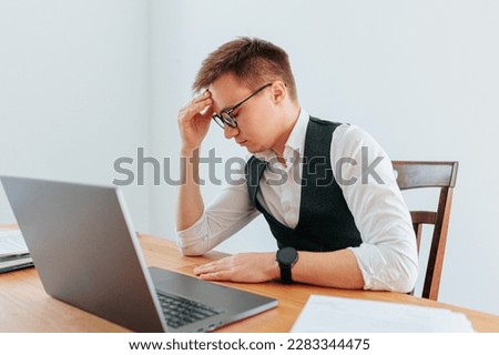 A guy in eyeglasses holds his head in his hands, feeling the weight of a headache and the stress of a long day at work. Headaches and Pressure The Strain of the Workplace