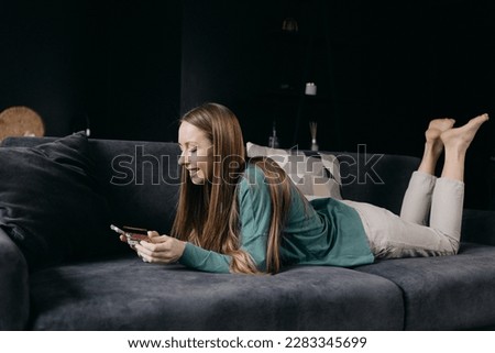 Young woman lying relaxing on sofa use phone make online payment with credit card, female rest on couch at home shopping on internet, secure banking service system concept. High quality photo